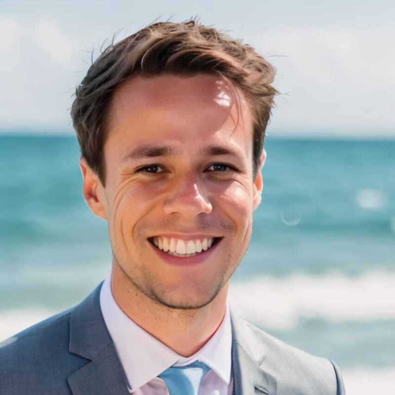 Foto de um especialista em marketing digital sorrindo, vestindo um terno cinza claro e gravata azul, com o mar ao fundo. A imagem será utilizada para ilustrar citações de um especialista em marketing digital.