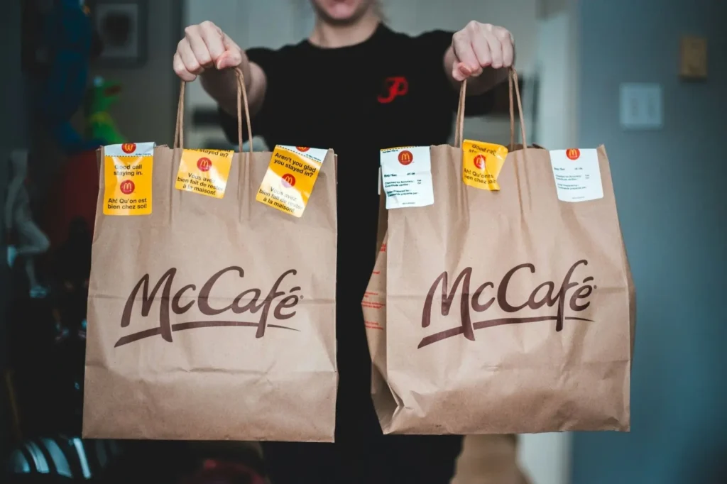 Atentendente de restaurante fast food segurando duas sacolas do McCafé.