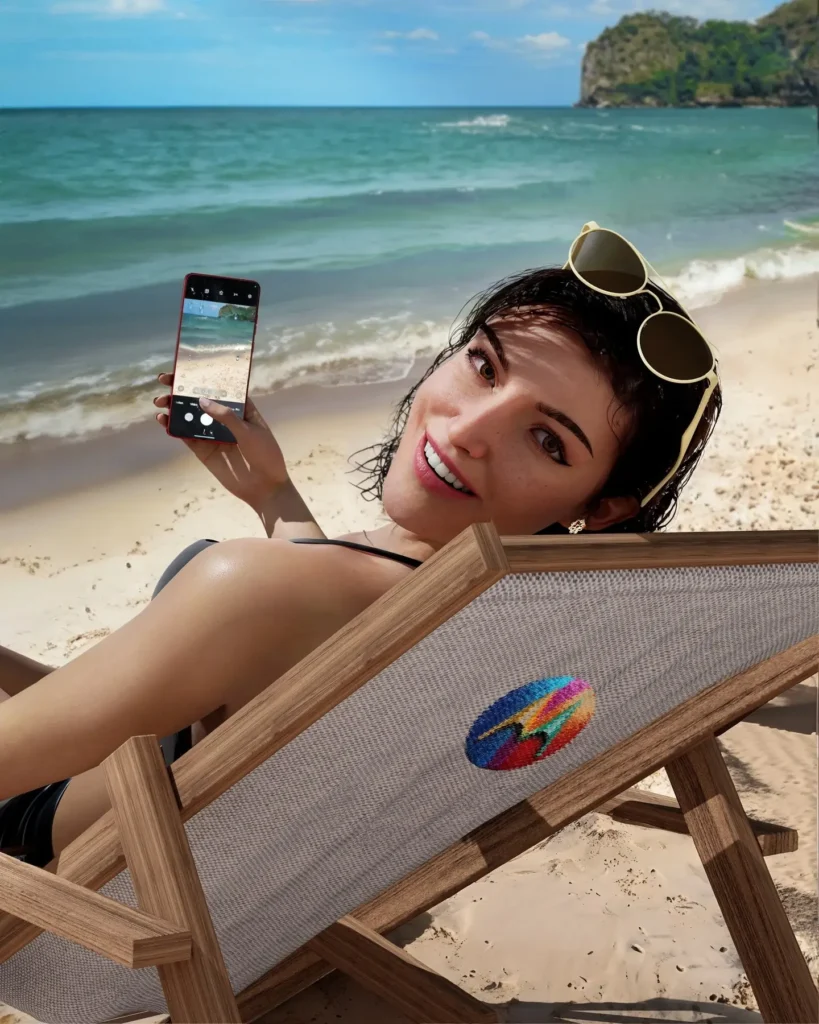 Lu do Magalu na praia olhando para a camera e mostrando celular, sentada numa cadeira de praia com a logo da Motorola.