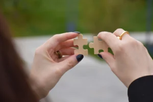 Mãos femininas montando duas peças de quebra-cabeças ilustrando a peça que faltava na sua estrutura corporativa em texto sobre estratégia de marketing.