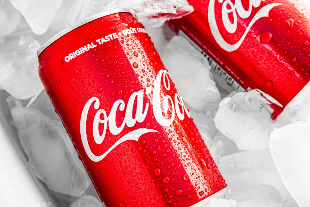 Duas latas vermelhas de Coca-Cola com cubos de gelo ao fundo.