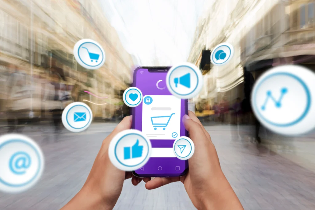 Mãos seguram um smartphone que mostra acarrinho de compras de app roxo e emojis saindo da tela