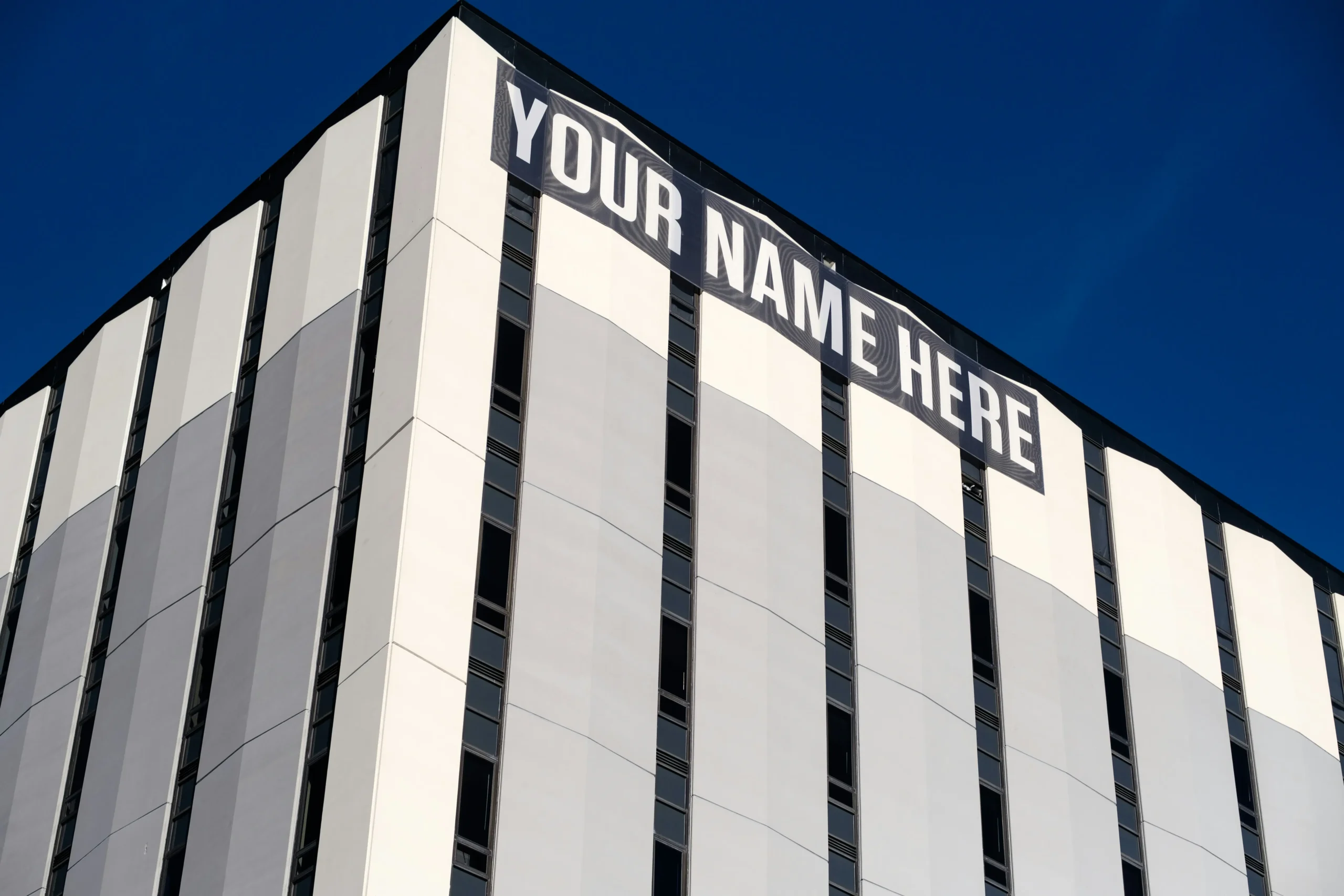 Edifício visto de baixo com faixa no topo dizendo "Your Name Here" ("Seu Nome Aqui" em português)