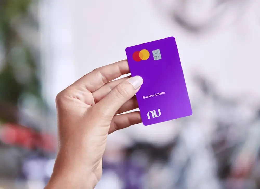 Mão feminina segurando o cartão roxo do Nubank
