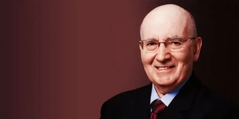 Foto de Philip Kotler sob fundo vermelho escuro. Ele veste terno preto, gravata vermelha e usa óculos.