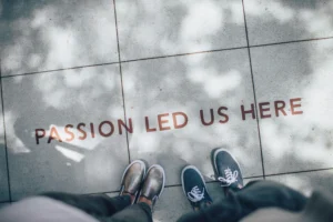 Foto de uma calçada com dois pares de pés ao lado da frase "Passion led us here" (paixão nos trouxe até aqui, em português).