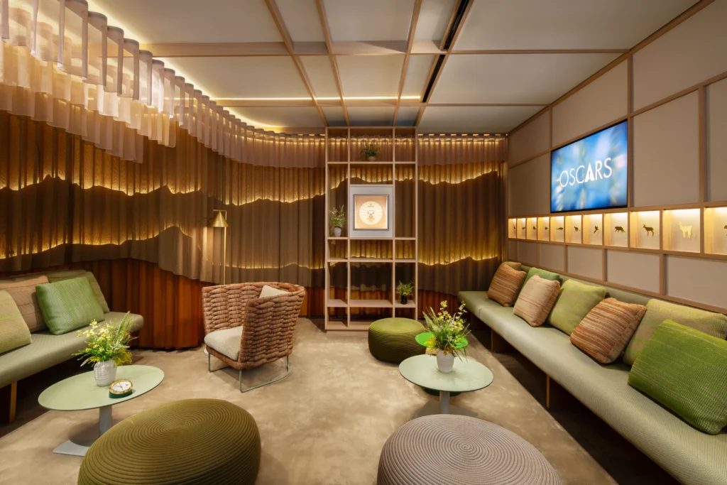 Sala da Rolex em tons de cinza, marrom e verde com uma televisão mostrando a apresentação do Oscar.
