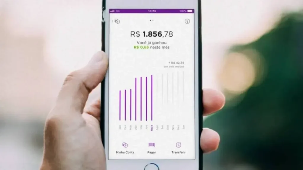 Mão segurando celular com aplicativo do Nubank aberto mostrando gráfico de investimentos.